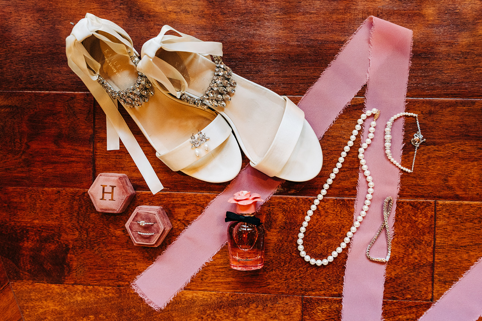 Detailed wedding day flatlay of wedding rings, shoes, perfume, jewelry and vow book.