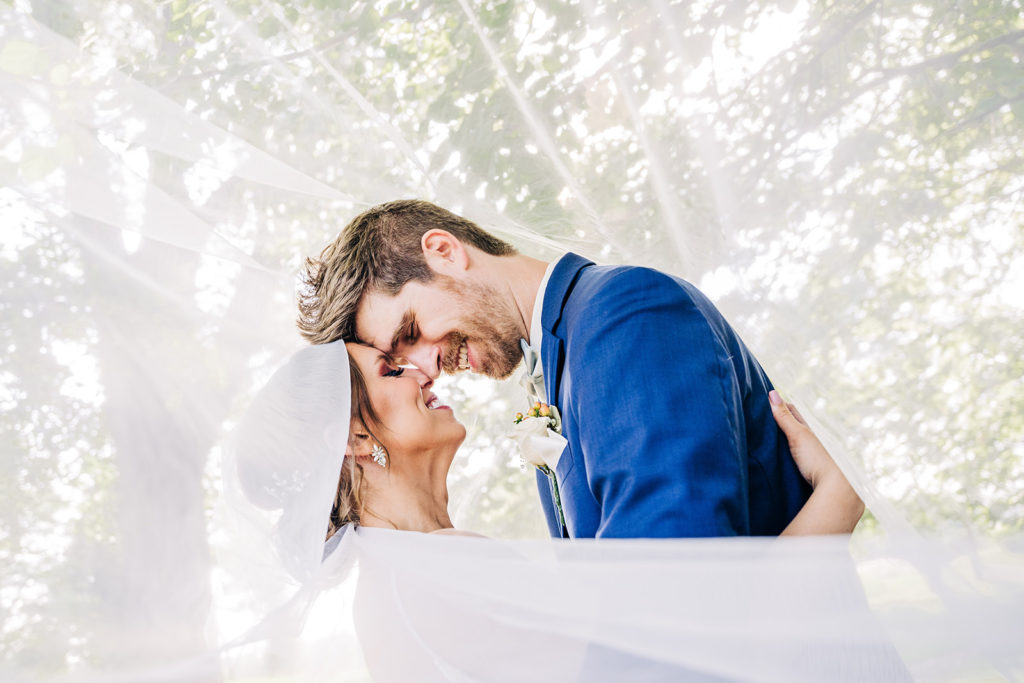 A couple embraces under a windblown veil during their wedding at Whippoorwill Hill.